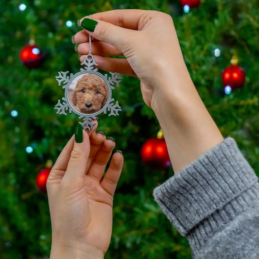 A person holding a printify Pewter Snowflake Ornament amidst holiday decor.