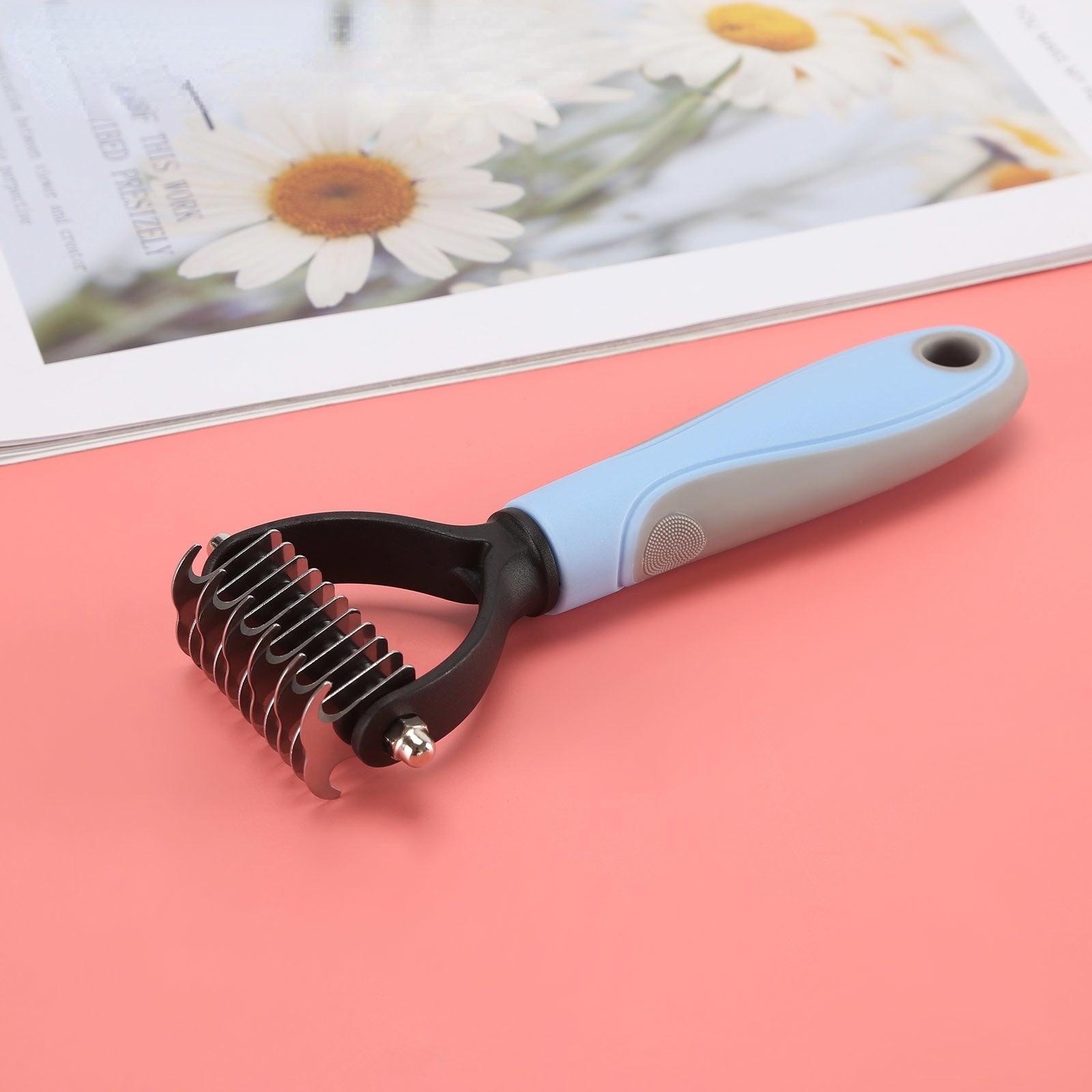 A blue and white Sweetest Paw Dog Comb Pet Hair Removal Comb on a pink background.